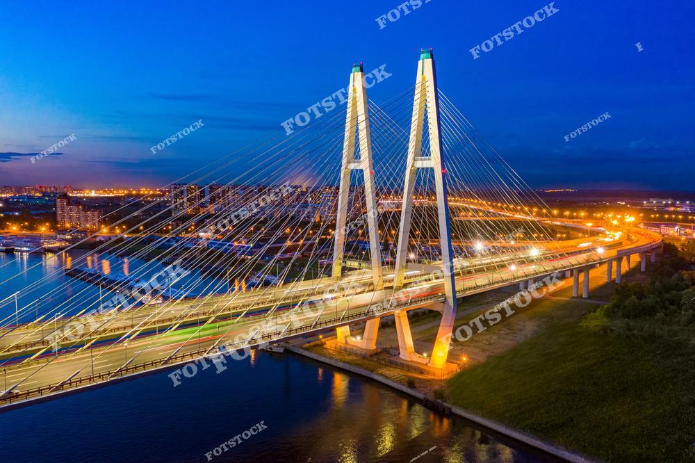 Фотография Санкт-Петербург, Россия, сделанная в период белых ночей. На изображении запечатлён Большой Обуховский мост — вантовый мост, раскинувшийся над рекой Нева. Фотоснимок передаёт атмосферу белых ночей: мягкий свет, отражения в воде и величественный силуэт моста. Фото подчёркивает популярность водных экскурсий по Неве и каналам Санкт-Петербурга, а также романтику путешествия по России в летний период. Иллюстрация может использоваться как изображение, картинка или слайд, посвящённые белым ночам и городским пейзажам Петербурга.